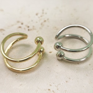 May include: Two ear cuffs are shown, one gold and one silver. Each cuff has a double-band design with a small ball detail at the top. The gold cuff is on the left, and the silver cuff is on the right.