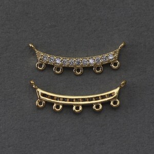 May include: Two gold-colored, curved jewelry components. The top piece is adorned with clear, round gemstones. Both pieces have small loops for attachment and are set against a dark gray background. These components are ideal for jewelry making.