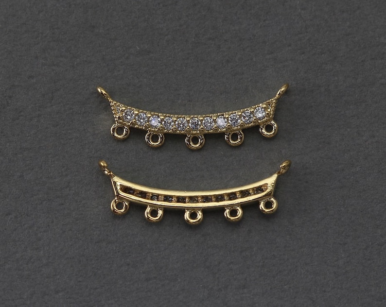 May include: Two gold-colored, curved jewelry components. The top piece is adorned with clear, round gemstones. Both pieces have small loops for attachment and are set against a dark gray background. These components are ideal for jewelry making.