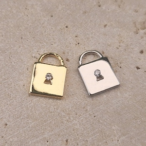 May include: Two lock charms, one gold and one silver, with a small clear rhinestone in the keyhole.