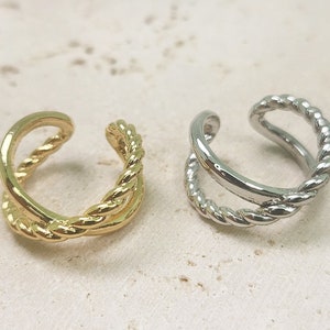 Könnte beinhalten: Zwei Ohrclips, einer in Gold und einer in Silber, mit einem gedrehten Seil-Design.