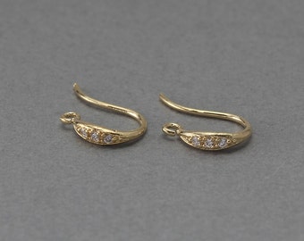 May include: A pair of gold earring hooks with a curved design and small clear stones set in the metal.