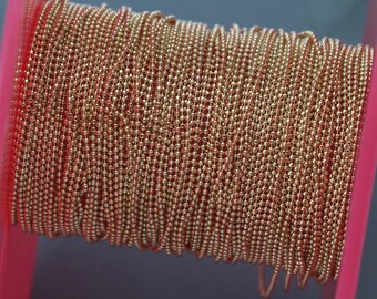 May include: A spool of gold-colored ball chain. The chain is wound tightly around the spool, which is pink.