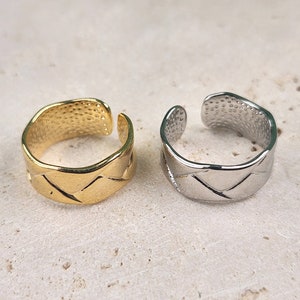 Könnte beinhalten: Zwei verstellbare Ringe, einer golden und einer silbern, mit einem geflochtenen Design. Die Ringe haben eine strukturierte Oberfläche.