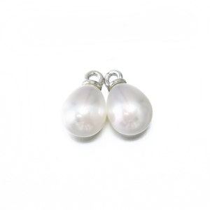 May include: Two white pearl teardrop charms with silver loops. The pearls are smooth and have a slight iridescent sheen.