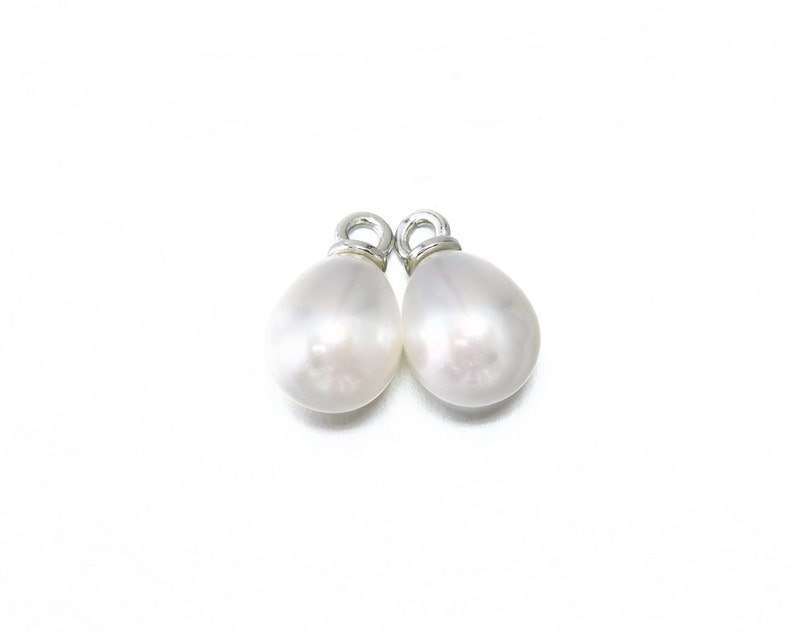 May include: Two white pearl teardrop charms with silver loops. The pearls are smooth and have a slight iridescent sheen.