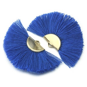 Puede incluir: Dos flecos de borla azul con detalles en forma de semicírculo de metal dorado. Las borlas están abiertas en abanico y los detalles metálicos están unidos a la parte superior de las borlas.