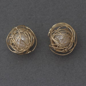 May include: A pair of gold earrings with a pearl in each, enclosed in a delicate wire cage design.