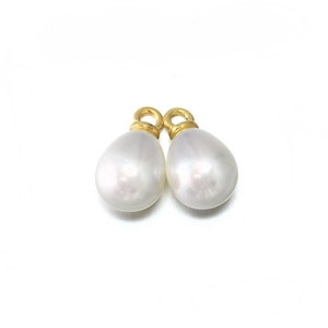 May include: Two white pearl teardrop charms with gold jump rings. The pearls are smooth and have a slight iridescent sheen.