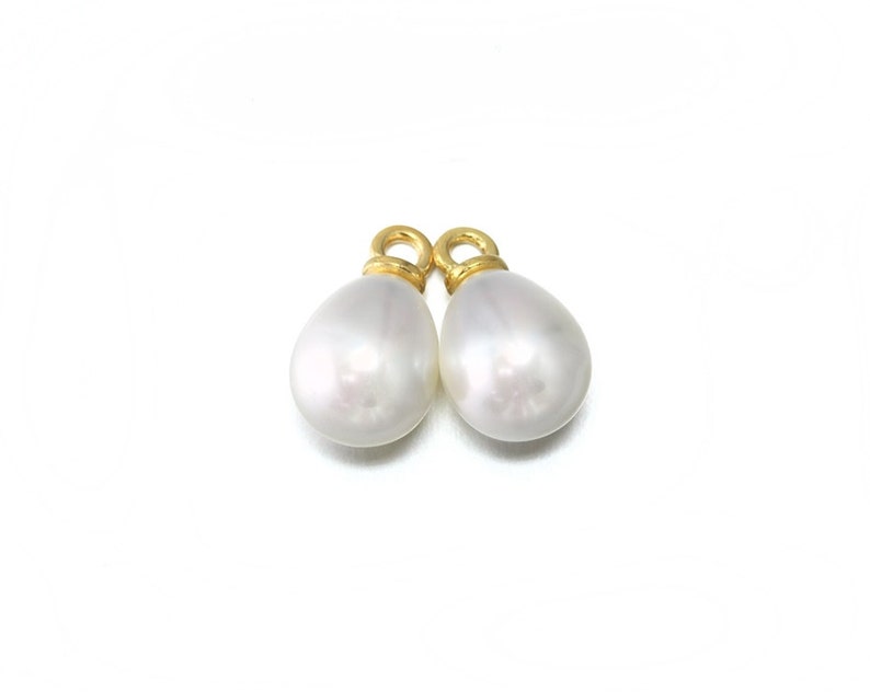 May include: Two white pearl teardrop charms with gold jump rings. The pearls are smooth and have a slight iridescent sheen.