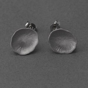 May include: A pair of silver stud earrings with a textured, flower-shaped design.