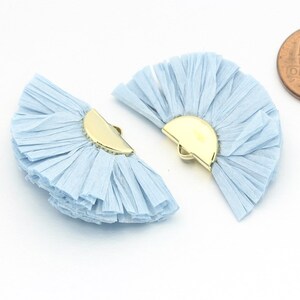 May include: Two light blue paper fan embellishments with gold metal accents. The fans are made of thin strips of paper that are layered and fanned out to create a delicate and airy look.