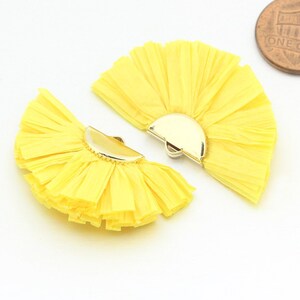 May include: Two yellow fabric fan-shaped earrings with gold metal accents. The earrings are layered and have a fringed texture.