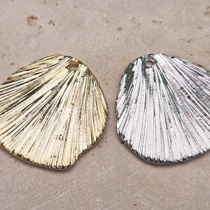 May include: Two metal shell-shaped charms, one gold and one silver, with a textured design and a hole for hanging.