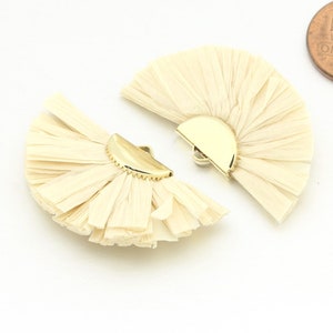 May include: Two beige straw fan-shaped embellishments with gold metal accents. The embellishments are approximately 5 cm in diameter.