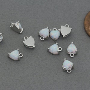 Könnte beinhalten: Zehn silberne herzförmige Anhänger mit weißen Opal-Steinen. Jeder Anhänger hat eine Öse zum Anbringen an Schmuck.