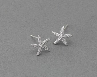 May include: A pair of silver starfish earrings. The earrings are small and delicate, and they have a sparkly finish.