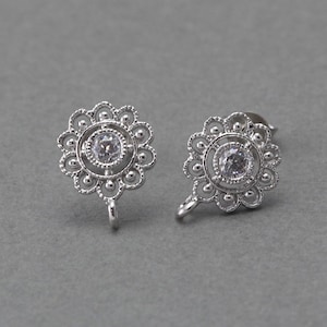 Puede incluir: Un par de pendientes de plata con un delicado diseño floral y un cristal transparente en el centro. Los pendientes tienen un cierre de gancho.