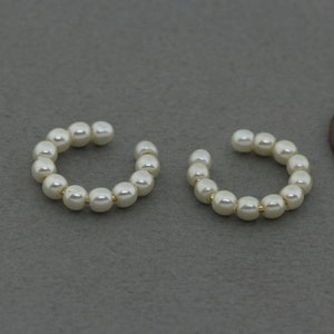 May include: A pair of pearl ear cuffs. Each cuff is made of a circle of small white pearls connected by a thin gold wire.