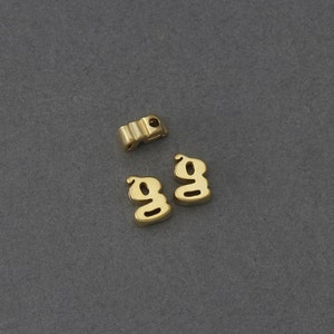 May include: Two gold-colored letter G charms. The charms are made of metal and have a slightly raised design.