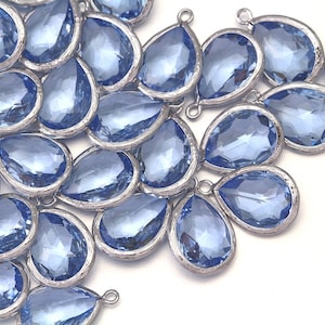 May include: A collection of light blue teardrop-shaped glass beads with silver-toned metal accents. The beads have a faceted design and are strung together with a loop at the top.