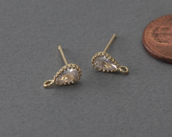 May include: A pair of gold-tone earring posts with a teardrop-shaped clear crystal and a small loop at the bottom.