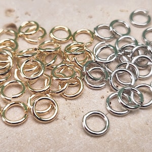 Puede incluir: Un montón grande de anillos de salto dorados y plateados. Los anillos de salto son anillos metálicos circulares pequeños que se utilizan para conectar componentes de joyería.