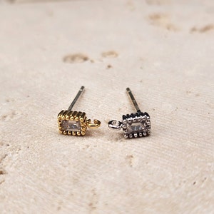 May include: Two earring posts with a square-shaped clear crystal set in a gold and silver frame. Each earring has a small loop for attaching a charm.