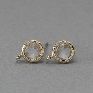May include: A pair of gold earrings with clear faceted gemstones. The earrings have a textured, hammered finish.