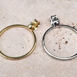 May include: Two hoop earrings, one gold and one silver, with a simple circular design. The earrings are shown on a light brown textured surface.