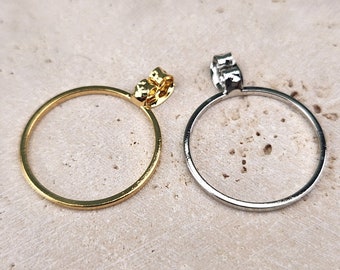 May include: Two hoop earrings, one gold and one silver, with a simple circular design. The earrings are shown on a light brown textured surface.