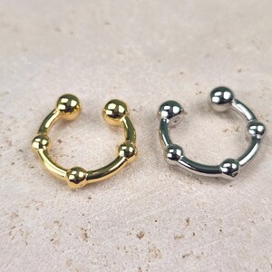 May include: Two non-pierced ear cuffs, one gold and one silver, with a rounded, slightly curved shape and five small round beads.