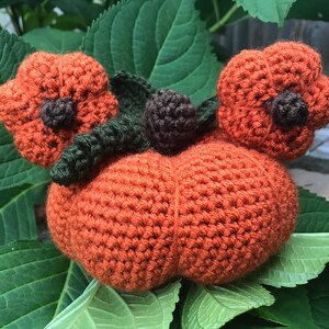 May include: A crocheted pumpkin with two smaller pumpkins on top, all in orange. The pumpkins have brown stems and green leaves.