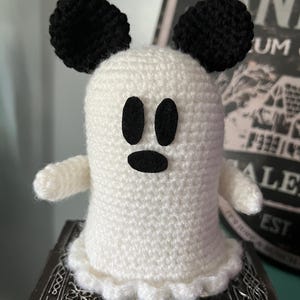 May include: A handmade crochet ghost in white with black eyes, mouth, and ears. The ghost has small arms and a ruffled bottom edge. The ghost is sitting on a decorative box. A fun Halloween decoration.