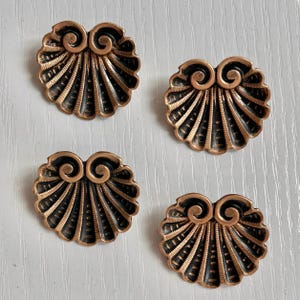 May include: Four antique copper-colored shell-shaped buttons with a black and gold design.