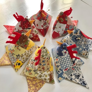 May include: Six colorful patchwork pincushions shaped like chickens. Each pincushion is made of different fabrics in shades of blue, red, yellow, and white. The pincushions have red felt beaks and yellow felt feet.