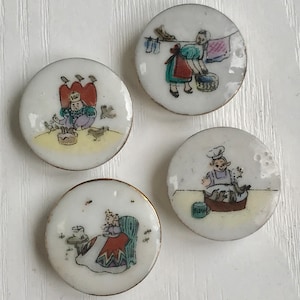 May include: Set of four white ceramic buttons with gold trim. Each button features a different illustration of a person and birds. One button shows a person in a crown feeding birds, another shows a person hanging laundry, another shows a person feeding birds from a bowl, and the last shows a person feeding birds from a bucket.