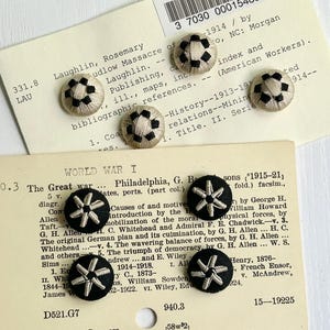 May include: A collection of vintage buttons with intricate designs. Some buttons feature a soccer ball pattern in black and beige, while others display a starburst design in silver on a black background. The buttons are arranged on aged index cards.