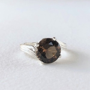 May include: A silver ring with a brown gemstone set in a swirl design.