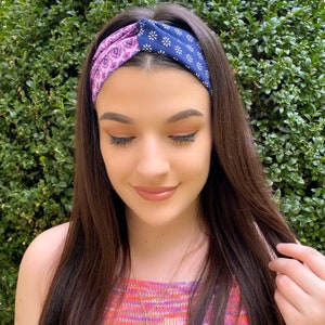 May include: A woman with long brown hair is wearing a blue and purple patterned headband. The headband is twisted and tied at the top of her head.