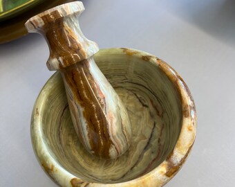 May include: A green and brown marble mortar and pestle set. The mortar is a bowl shape with a wide rim and the pestle is a rounded cylinder.