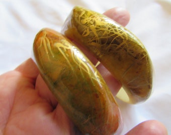 May include: Two thick, rounded, green and gold bangles with a marbled effect and gold flecks.