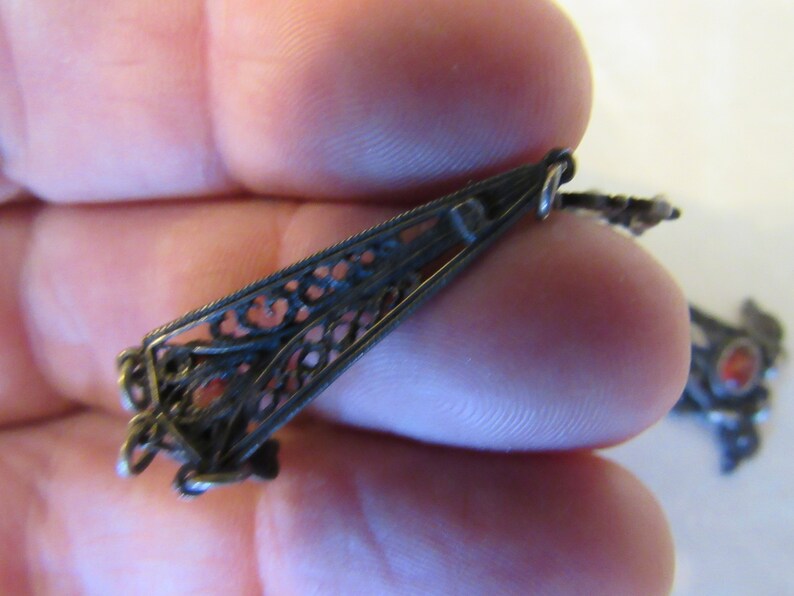 Op de afbeelding: Een zilveren filigraan hanger met een rode steen. De hanger is bevestigd aan een ketting met een zilveren sluiting.
