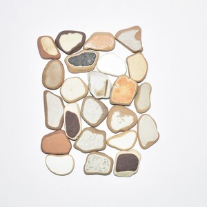 May include: A collection of smooth, flat, irregularly shaped stones in various shades of brown, white, and black. The stones are arranged in a square shape.