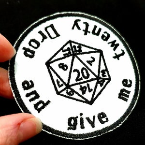 Op de afbeelding: Witte geborduurde patch met zwarte tekst en een zwart-witte geborduurde 20-zijdige dobbelsteen. De tekst luidt "Give me and drop" en "twenty".