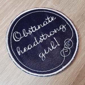 Peut inclure: Un patch rond bleu marine avec une broderie blanche qui dit "Obstinate headstrong girl!"