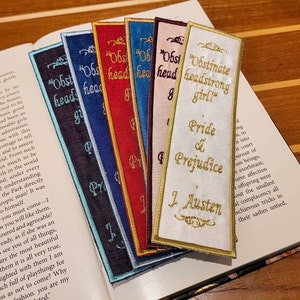 Peut inclure: Un ensemble de six marque-pages colorés avec du texte brodé. Les marque-pages présentent les titres de romans classiques, notamment "Orgueil et Préjugés", "Fille obstinée et entêtée" et "Raison et Sentiments".