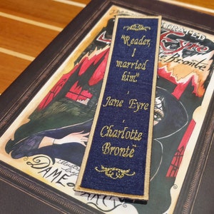 Op de afbeelding: Een blauwe stoffen bladwijzer met gouden borduurwerk. De bladwijzer bevat een citaat uit Jane Eyre van Charlotte Brontë: "Lezer, ik heb hem getrouwd."