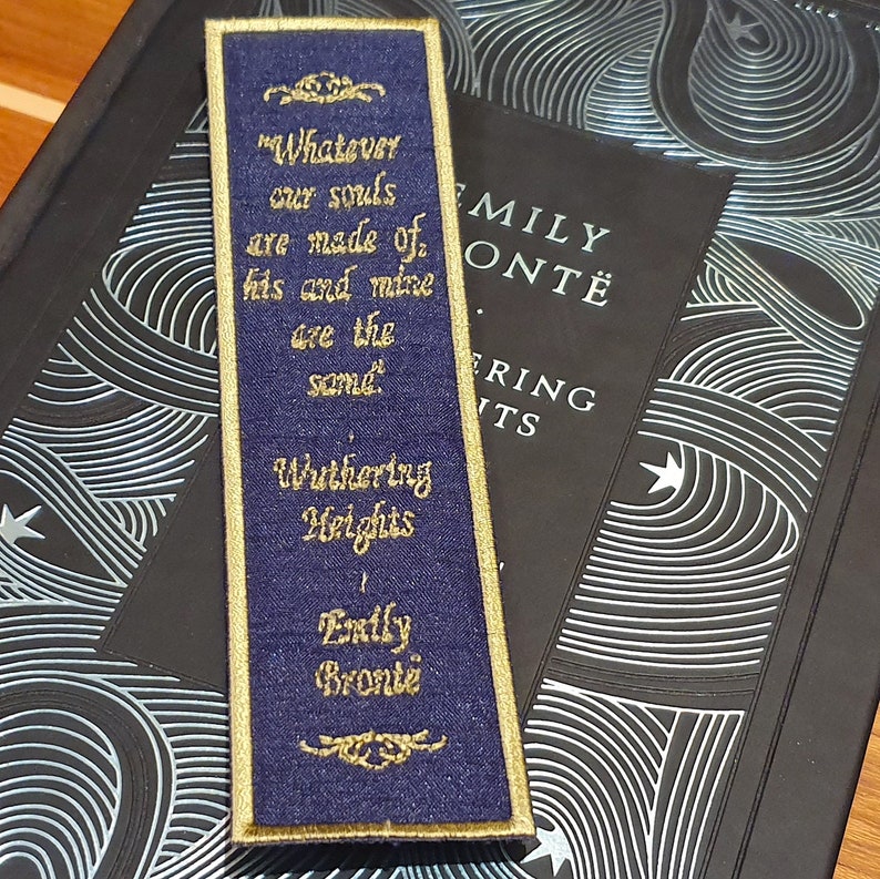 May include: A blue bookmark with gold embroidery featuring a quote from Emily Bront&euml;'s Wuthering Heights: "Whatever our souls are made of his and mine are the same."