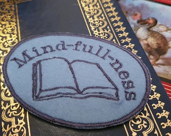 Peut inclure: Un patch brodé bleu avec le texte "Mindfulness" et un dessin de livre ouvert.
